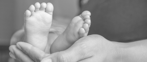 Pés de um bebê apoiados por uma mão de uma pessoa adulta