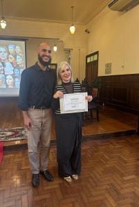 O arte educador Whiverson entrega o certificado de participação para a convidada.