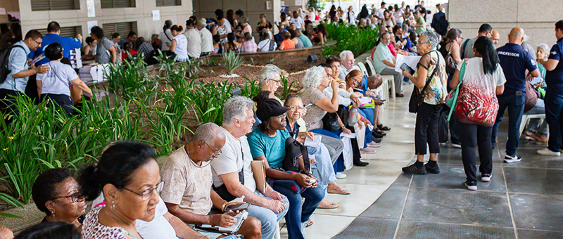 Pesoas sentadas, enfileiradas, e outras em pé durante atendimento do evento 