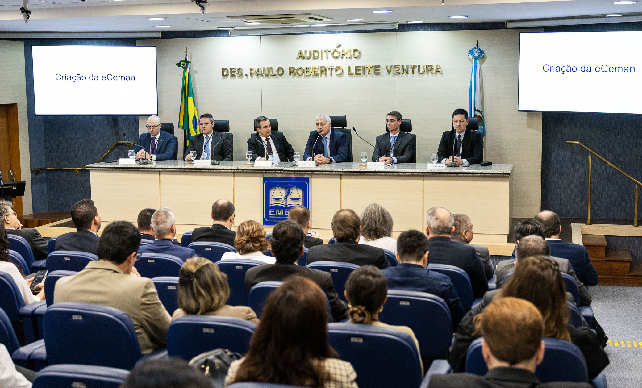 Foto do Auditório Des. Paulo Roberto Leite Ventura com seis debatedores sentados na mesa principal e a plateia com homens e mulheres. 