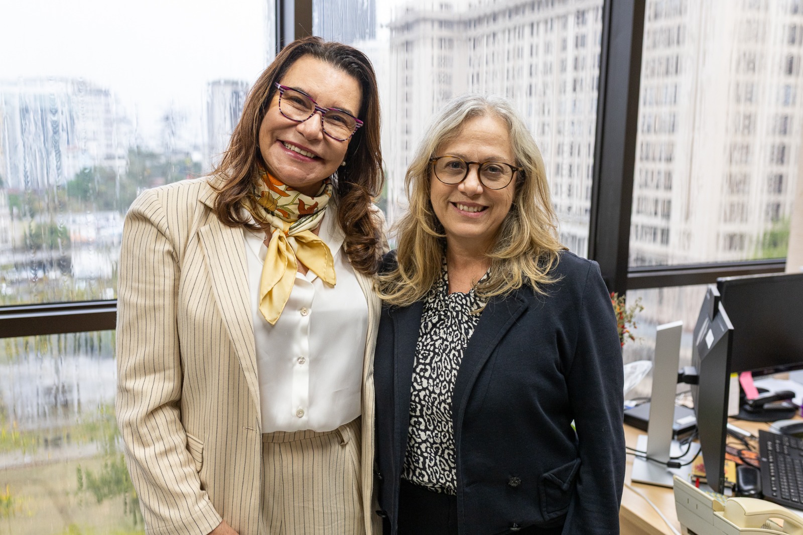 As juízas Gisele Guida e Marcia Capanema posam para foto em pé no gabinete da Vara Especializada em Crimes contra a Criança e o Adolescente
