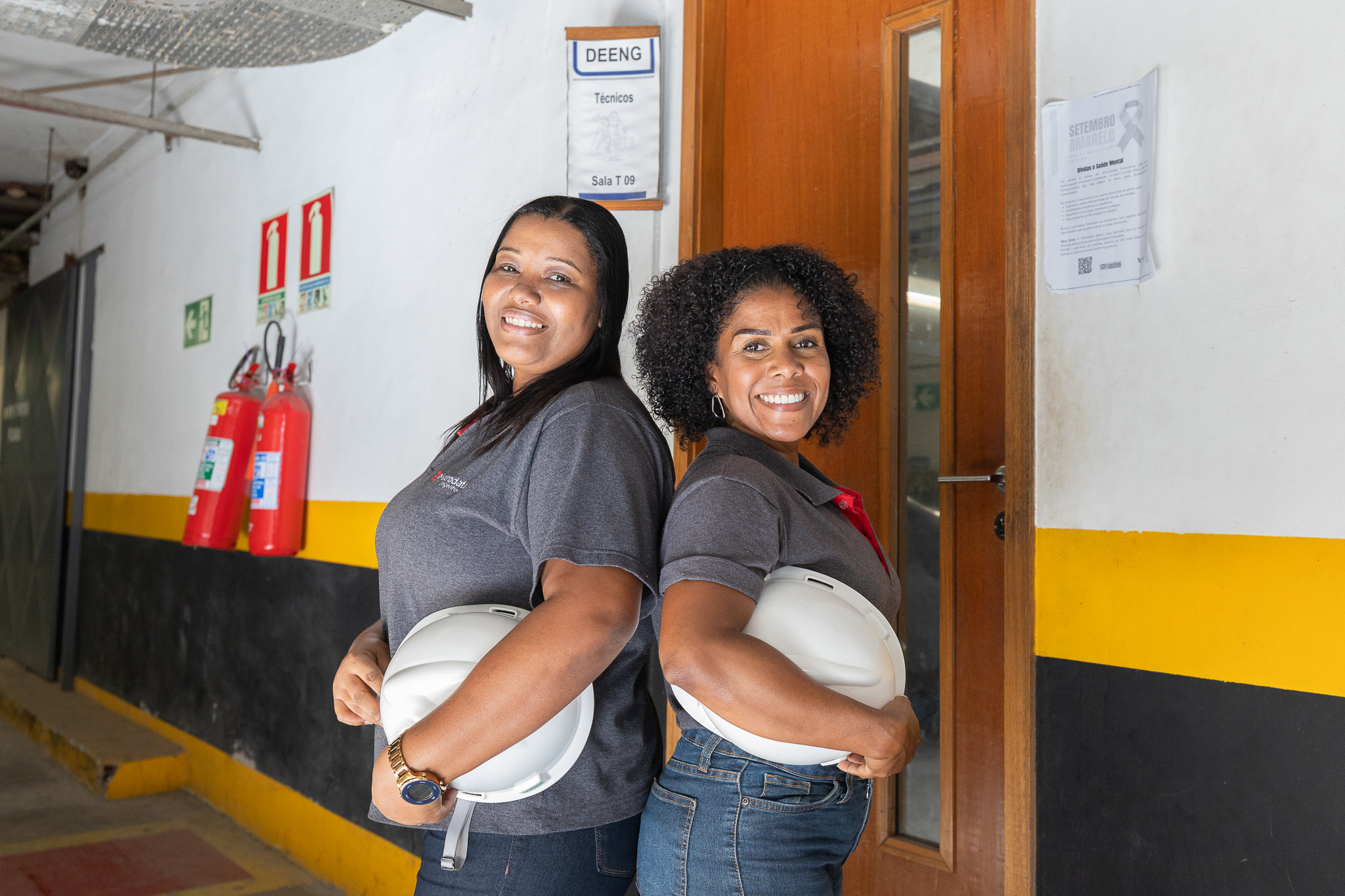 A imagem mostra duas mulheres segurando capacetes de obra 