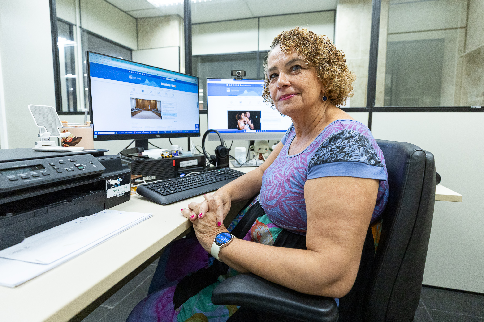A servidora Maria Eugênia posa para a foto sentada na sua estação de trabalho.