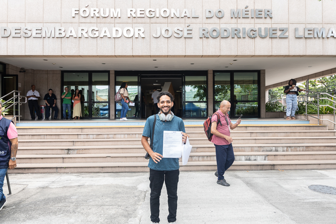Artur Xavier posa na fachada do Fórum do Méier com um papel de indicação para uma vaga de emprego em um shopping em Guadalupe