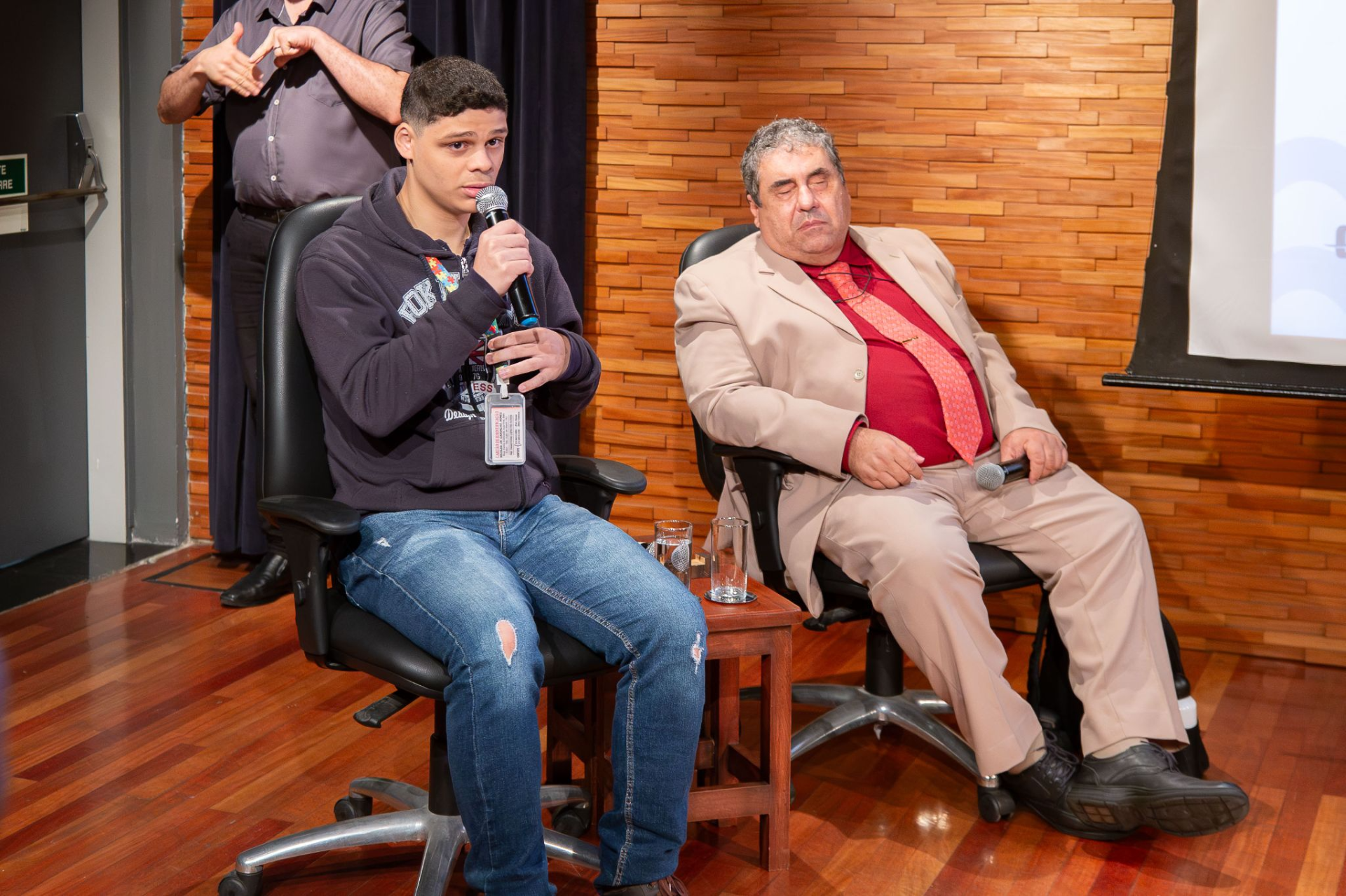 Imagem de Nicolas Nunes sentado com microfone e Marcio Aguiar