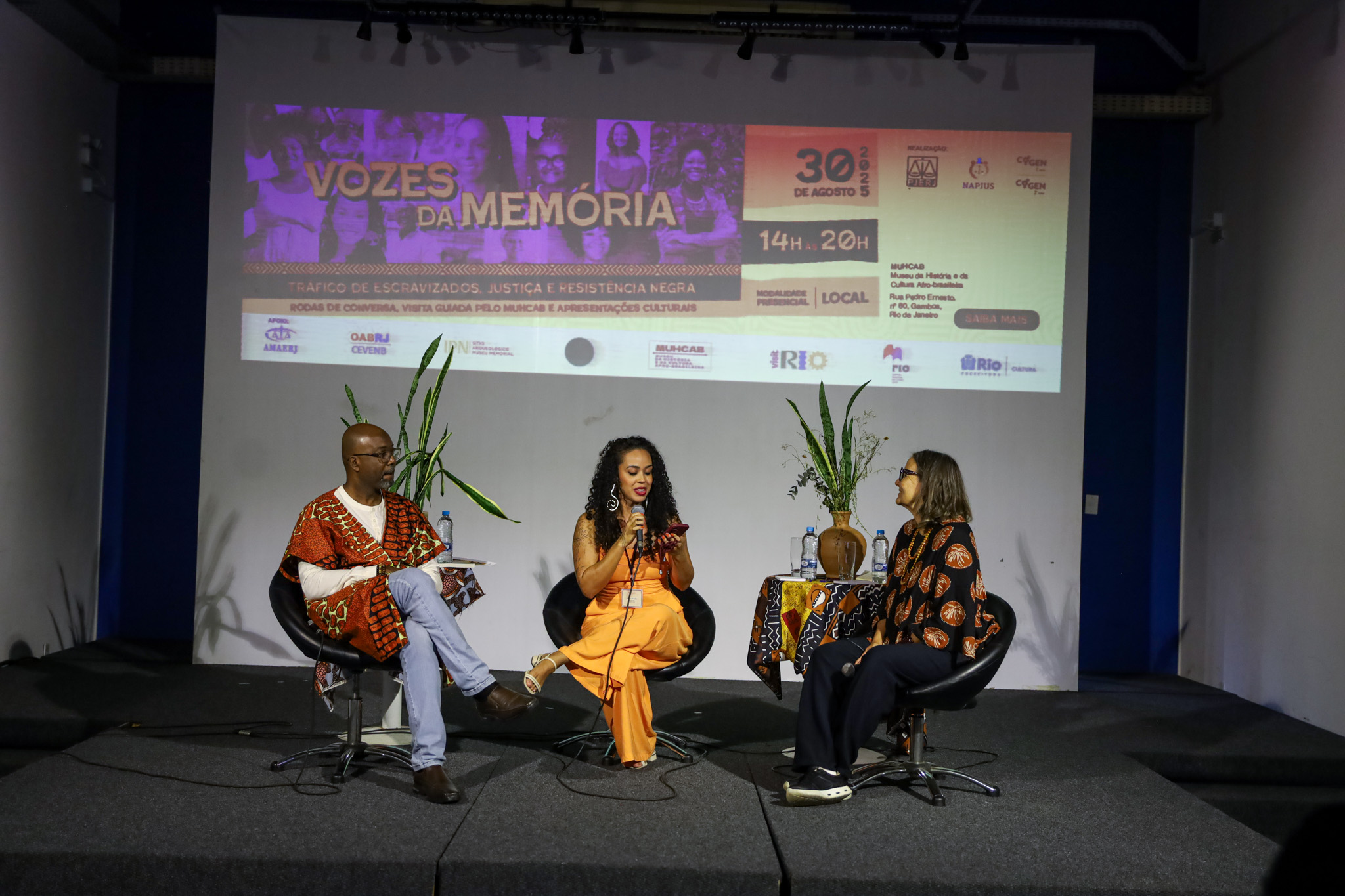 ​ to. A ação foi promovida pelo Núcleo de Apoio e Promoção à Justiça Social (Napjus), integrante dos Comitês de Promoção da Igualdade de Gênero e de Prevenção e Enfrentamento do Assédio Moral e Sexual e da Discriminação (Cogens 1º e 2º Graus) do Tribunal de Justiça do Rio de Janeiro (TJRJ). O evento reuniu magistrados, servidores, professores e o público em geral para debater os reflexos que o processo de escravidão ocasionou na sociedade brasileira.    O presidente do Cogen 1º Grau, desembargador Wagner Cinelli, representou o presidente do TJRJ, desembargador Ricardo Couto de Castro, e abriu o encontro ao lado da presidente do Cogen 2º Grau, desembargadora Patricia Serra, reafirmando a missão do Napjus. “O Núcleo de Apoio e Promoção à Justiça Social atua no Pacto Nacional do Judiciário pela Equidade Racial a fim de prevenir a discriminação racial. E uma das formas de fazermos isso é pela promoção de diálogos, palestras e ações que gerem reflexões na sociedade”, destacou.    A desembargadora Patricia Serra também destacou o papel do Judiciário de compreender a realidade e ser um garantidor da Justiça. “O evento de hoje passa por temas sensíveis, como o tráfico de escravizados. Uma das consequências desse período foi o racismo ambiental, que afasta a população majoritariamente negra e pobre para as margens da sociedade. Precisamos ter uma política pública acertada que vá contra isso, e esse é um dos papéis do Poder Judiciário, o de promover o acesso aos Direitos e à Justiça Social”, ponderou.    A gestora pelo TJRJ do Pacto Nacional do Judiciário pela Equidade Racial, juíza Leidejane Chieza, pontuou um dos objetivos da iniciativa. “Vozes da Memória foi pensado para reafirmar que preservar a história do povo negro é garantir dignidade, identidade e justiça para as próximas gerações”.         A primeira mesa foi mediada pela servidora Tatiana Brandão (ao centro) e palestrada pelos professores Júlio Cesar Pereira (à esquerda) e Marta Abreu (à direita)   ​