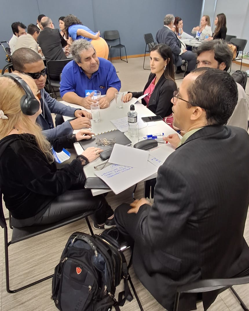 Pessoas portadoras de deficiência estão reunidas, sentadas em mesas redondas diferentes, em uma ampla sala na sede do CNJ, em Brasília, , e debatendo sugestões para a Política Nacional das Pessoas com Deficiência em Âmbito Judicial