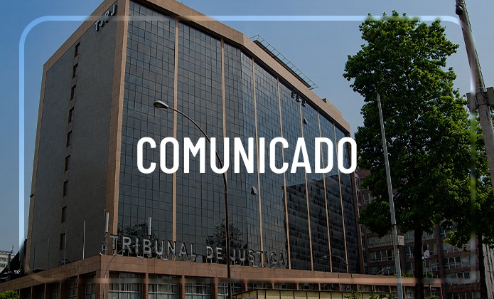 Imagem institucional apresenta a fachada de um edifício do Tribunal de Justiça, com vários andares e grandes painéis de vidro. Na parte inferior da construção, aparece a identificação “TRIBUNAL DE JUSTIÇA” em letras metálicas. Sobre a fotografia, há uma moldura azul-clara de cantos arredondados e, ao centro, a palavra “COMUNICADO”, escrita em letras brancas e maiúsculas. Em frente ao prédio, aparecem árvores, postes de iluminação e parte da via urbana. O céu está claro, e a composição utiliza a fotografia da sede do Tribunal como fundo para o comunicado institucional.