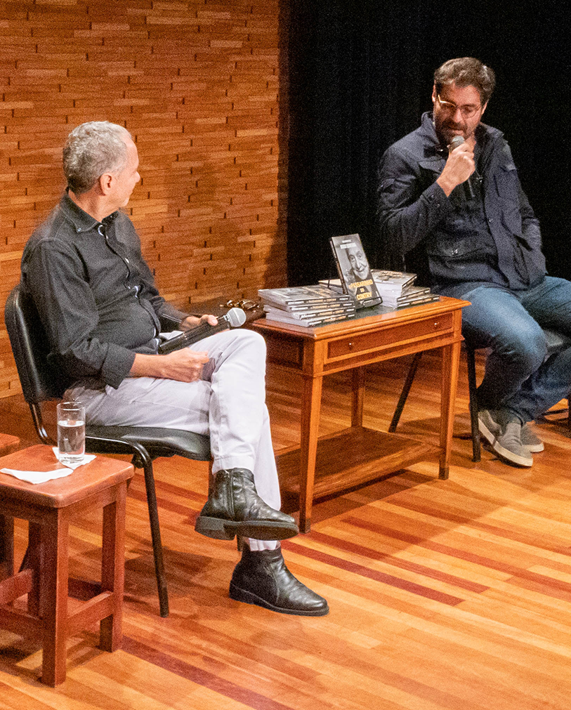 O desembargador Luís Gustavo Grandinetti e o ator Thiago Lacerda conversam sentados em cadeiras no palco da Sala Multiuso