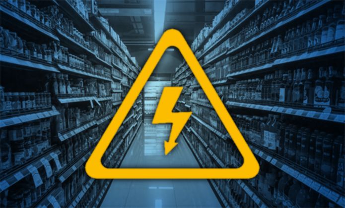 #ParaTodosVerem: Corredor de supermercado ou loja visto em perspectiva, com prateleiras cheias de produtos dos dois lados. Sobre a imagem, em destaque no centro, aparece um símbolo amarelo de advertência elétrica: um triângulo com um raio no interior, indicando risco de choque elétrico ou perigo relacionado à eletricidade em ambiente comercial ou de consumo.