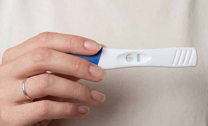 #ParaTodosVerem: Imagem em close mostra uma mão segurando um teste de gravidez com duas marcações visíveis no visor.